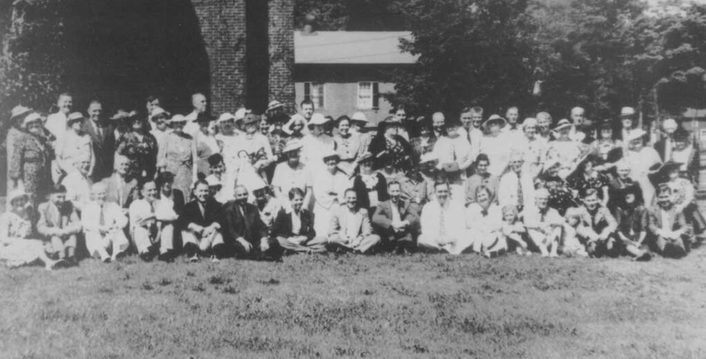 Black and white phot depicting a large gathering of people posing for the photographeron on a lawn